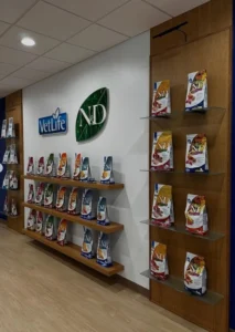 A modern retail display featuring pet food bags arranged on custom oak floating shelves against a white wall with oak wall panels and vertical slats.