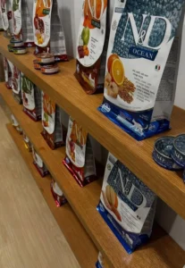 A close-up view of custom oak floating shelves displaying a variety of pet food bags. The shelves are neatly arranged, set against a white wall with a polished wooden floor, highlighting the craftsmanship and organized layout.