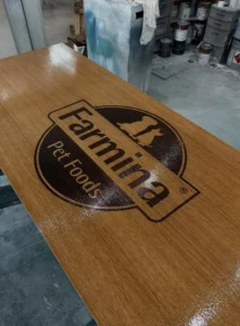 A close-up of a custom oak desk with a laser-etched Farmina Pet Foods logo, showcasing the glossy finish and detailed craftsmanship.