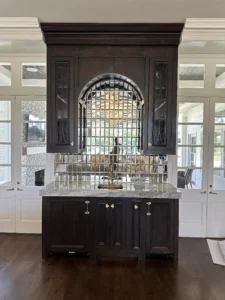 Custom stained cherry wet bar with built-in appliances, featuring glass cabinet doors with a solid cherry CNC-machined mullion and mirrored tile backsplash.