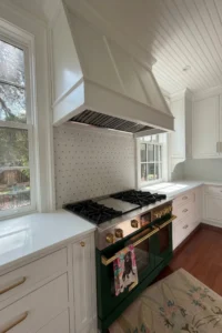 Custom white kitchen cabinetry with a large wood range hood, professional range, and detailed trimwork