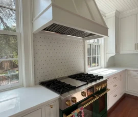 Custom white kitchen cabinetry with a large wood range hood, professional range, and detailed trimwork